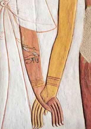 A photo taken inside the tomb of the Egyptian queen Nefertari. It shows the arms of two women with their hands clasped. The arm on the left belongs to Queen Nefertari and is painted a light brown; she also has a tattoo on the inside of her arm of the Eye of Ra. The arm on the right belongs to Hathor and is painted gold. 